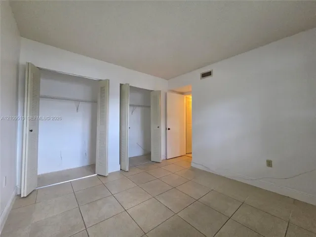 Room featuring large-format tile flooring, two closets with louvered bi-fold doors, and a solid-core interior door