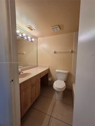 Bathroom featuring a vanity with wood-finish cabinetry, a solid surface integrated countertop, a full-width mirror with multi-bulb light fixture, and tile flooring