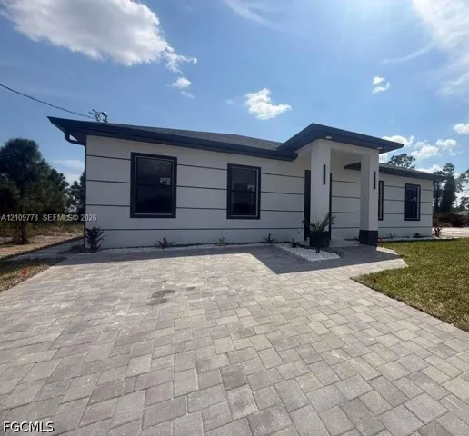 Modern exterior featuring white stucco finish with horizontal trim detailing, a covered entryway, and a paved brick driveway