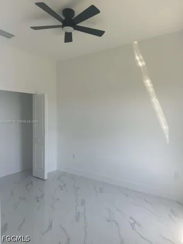 High-ceilinged room featuring large-format stone-finish tile flooring, matte black ceiling fan with integrated lighting, and a bi-fold door