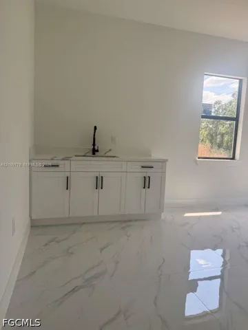 Wet bar featuring white cabinetry, a solid-surface countertop with an integrated sink, and a matte black faucet, complemented by polished stone-finish floor tile