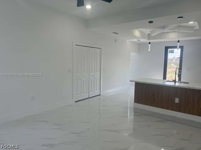 Interior space featuring polished porcelain tile flooring, tray ceiling with recessed lighting, kitchen island with slatted wood detailing and stone-finish countertop, dual pendant lights, and double-panel closet doors