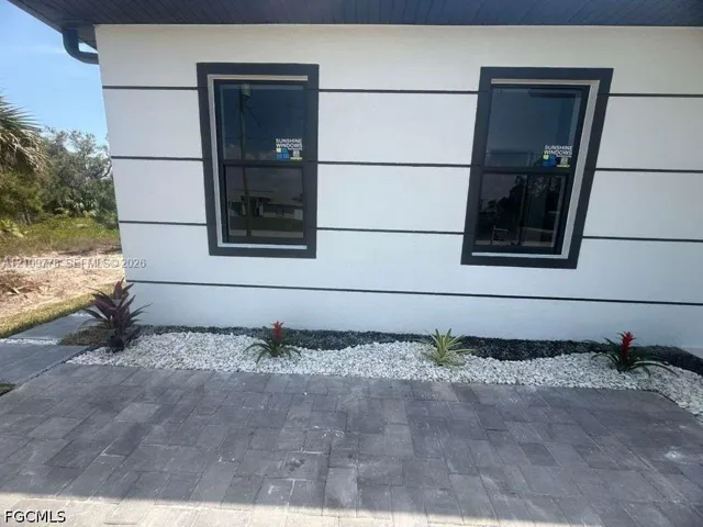 Exterior facade featuring white stucco finish with dark trim accents, double-hung windows, and paver hardscaping