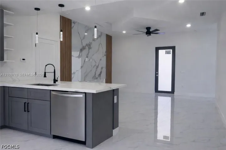 Kitchen featuring a stone-finish island countertop, matte black faucet, stainless steel dishwasher, full-height decorative wall paneling, and polished tile flooring