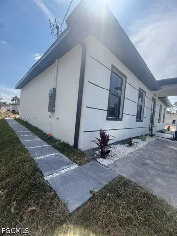 Exterior featuring a smooth-stucco facade with horizontal architectural banding, dark-trimmed windows, a paved walkway, and decorative rock landscaping