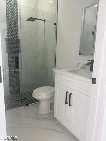 Bathroom featuring a white vanity with matte black hardware, a walk-in shower with glass enclosure, oversized wall and floor tiles, mosaic tile shower accents, and a rainfall showerhead