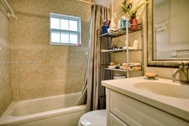 Bathroom featuring a shower-tub combination, tiled wall surrounds, a vanity with an integrated basin, and a framed wall mirror
