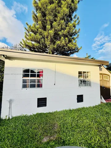Exterior white masonry wall featuring two grid-pane windows, dark-toned shutters, and a rear storage structure with paneled doors