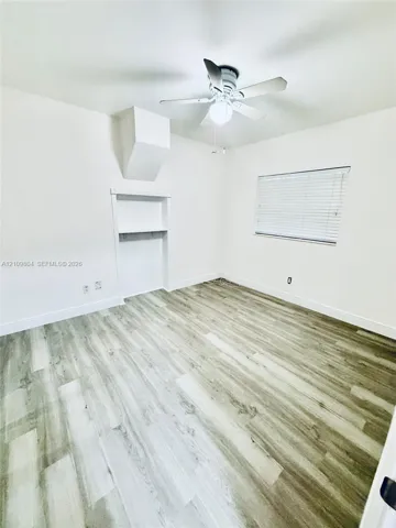 Room featuring wood-finish flooring, a built-in recessed storage niche, a ceiling fan with integrated lighting, and a window with horizontal blinds