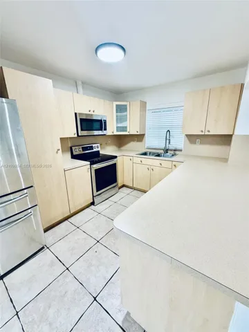 Kitchen featuring light-finish cabinetry, stainless steel appliances, expansive countertops, dual-basin sink with a high-arch faucet, and tile flooring