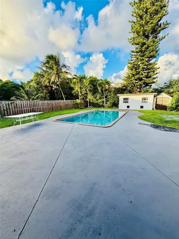 In-ground swimming pool with concrete decking, fenced perimeter, and detached storage structure