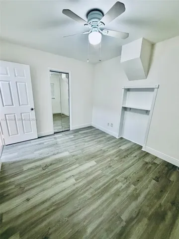 Room featuring wood-finish flooring, a ceiling fan with integrated lighting, a recessed wall niche with built-in shelving, and a closet with mirrored sliding doors