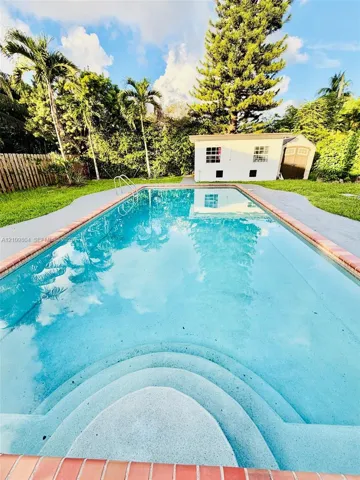Rectangular swimming pool featuring brick coping, integrated entry steps, and a concrete pool deck, set within a backyard with a detached storage structure