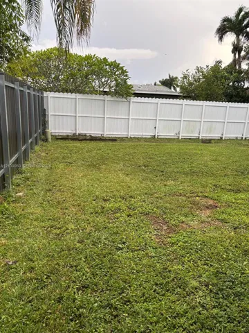Expansive backyard featuring a combination of white vinyl privacy fencing and metal perimeter fencing, mature trees, and a level lawn area