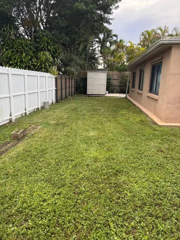 Side yard featuring a grass lawn, white vinyl fencing, mature trees, and a detached storage structure