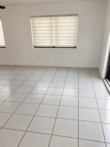 Neutral-toned interior space featuring light-colored ceramic tile flooring, off-white walls, and windows equipped with horizontal roller shades