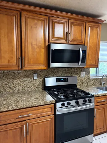 Kitchen featuring wood cabinetry with satin nickel pulls, natural stone countertops, a stainless steel gas range, and a built-in stainless steel microwave