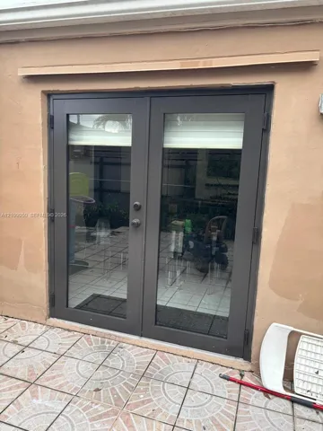 Double-pane glass French doors with dark metal frames and integrated locking hardware, set against a stucco exterior wall and patterned tile patio flooring