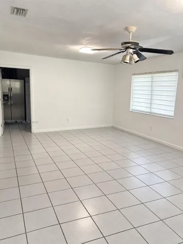 Open-concept interior featuring neutral tile flooring, a multi-light ceiling fan, and large-format window treatments