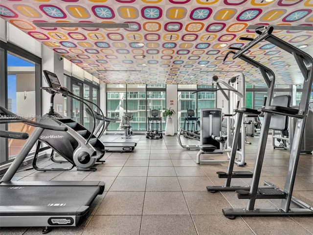 Fitness center featuring floor-to-ceiling windows, square tile flooring, and decorative patterned drop ceiling