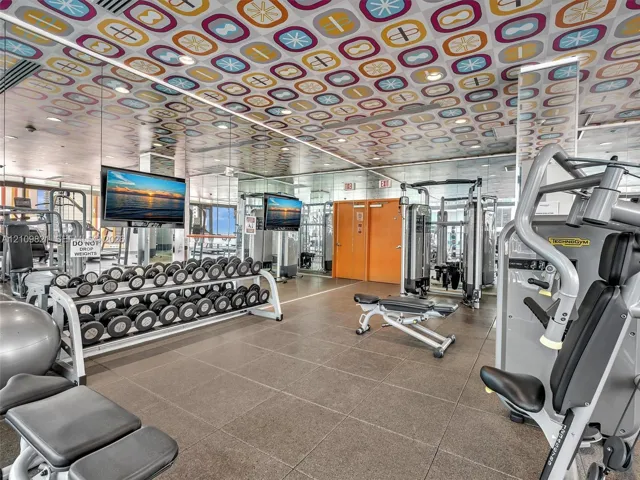 Fitness center featuring a patterned drop ceiling, neutral large-format floor tiles, recessed lighting, and mirrored wall panels