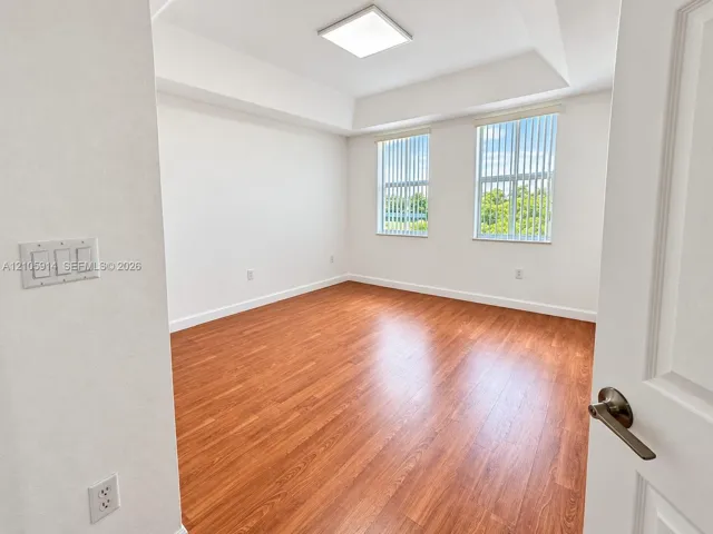 Room featuring wood-finish flooring, a tray ceiling, dual vertical windows, and a flush-mount overhead light fixture