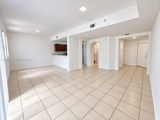 Open-concept interior featuring light-toned tile flooring, recessed lighting, a breakfast bar, and architectural arched detailing