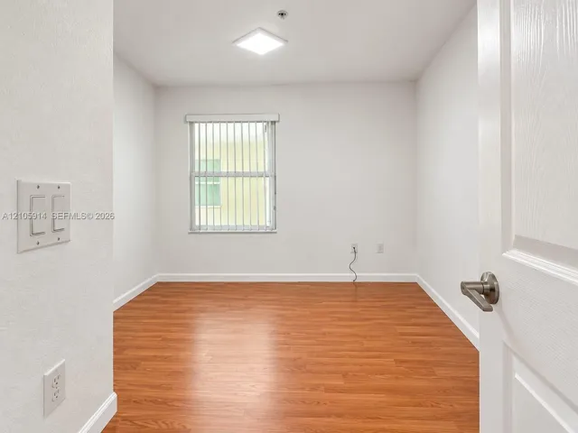 Room featuring wood-finish flooring, a flush-mount light fixture, and a window with vertical blinds
