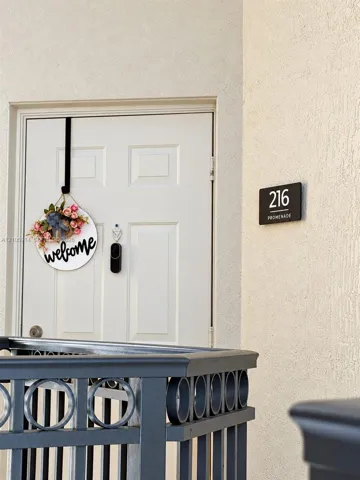 White paneled entry door with integrated peephole and smart doorbell camera, complemented by a matte finish metal railing featuring circular decorative detailing and a mounted address plaque