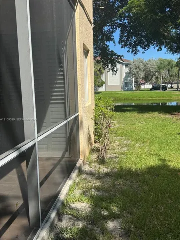 Screened-in enclosure with stucco exterior, manicured lawn, and water frontage