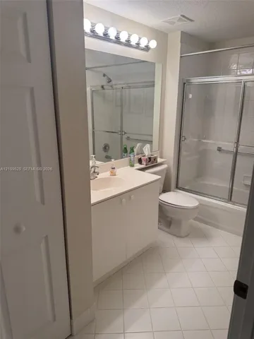 Bathroom featuring a vanity with a solid-surface countertop, a full-width mirror, an integrated sink, and a tub-and-shower combination with a sliding glass enclosure and tile flooring