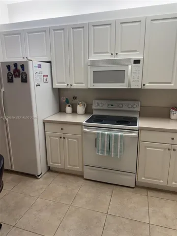 White Shaker-style cabinetry, solid-surface countertops, electric range, built-in microwave, and tile flooring