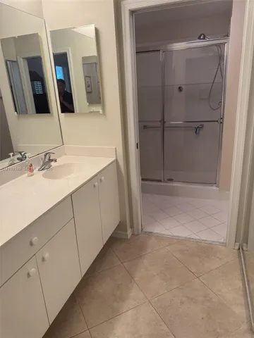 Bathroom featuring a long vanity with white cabinetry, a large wall-mounted mirror, and a walk-in shower with a sliding glass door and tile flooring