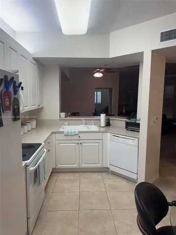 Kitchen featuring white cabinetry, solid surface countertops, an integrated double-basin sink, built-in dishwasher, and ceramic tile flooring