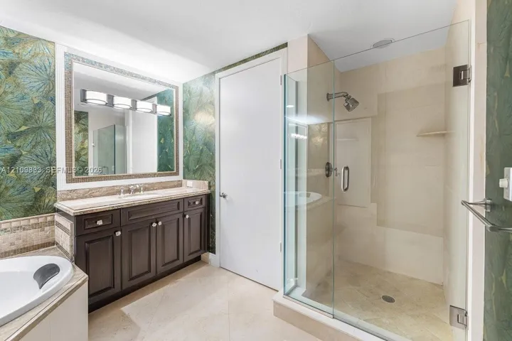 Dark wood cabinetry with stone-finish vanity top, glass-enclosed shower with tile surround, large-format tile flooring, and integrated soaking tub