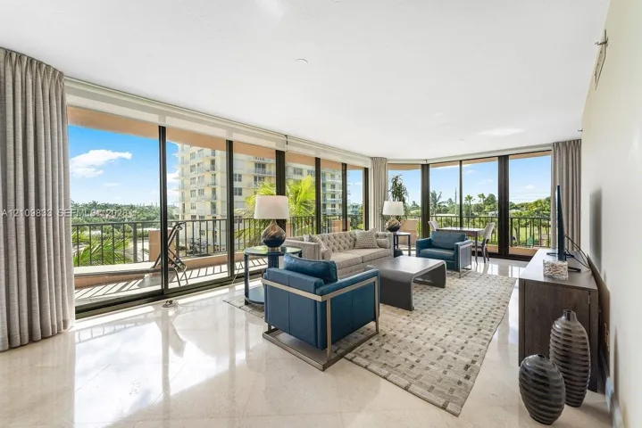 Floor-to-ceiling glass walls, polished stone flooring, and expansive wrap-around balcony with metal railing