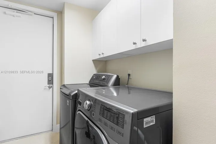 Laundry area featuring white built-in upper cabinetry with polished metal hardware and a solid-core entry door with a deadbolt lock