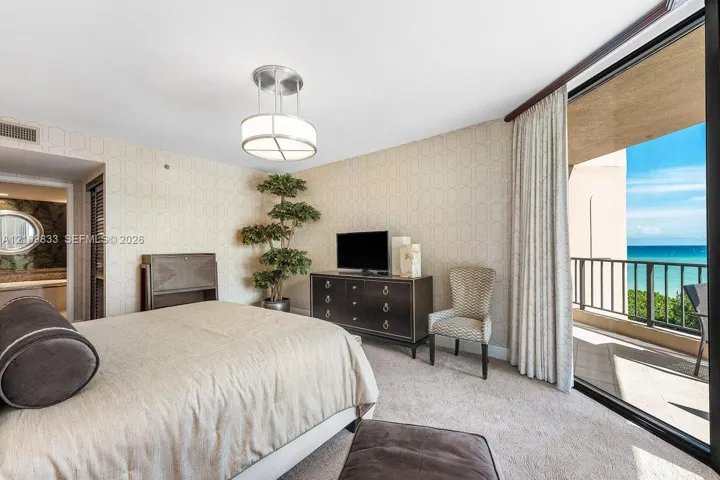 Textured wallcoverings, neutral carpeting, contemporary drum-style ceiling fixture, and full-height sliding glass doors leading to a private balcony with ocean backdrop