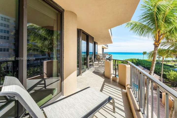Covered balcony featuring tile flooring, full-height glass sliding doors, and metal railings, overlooking the ocean