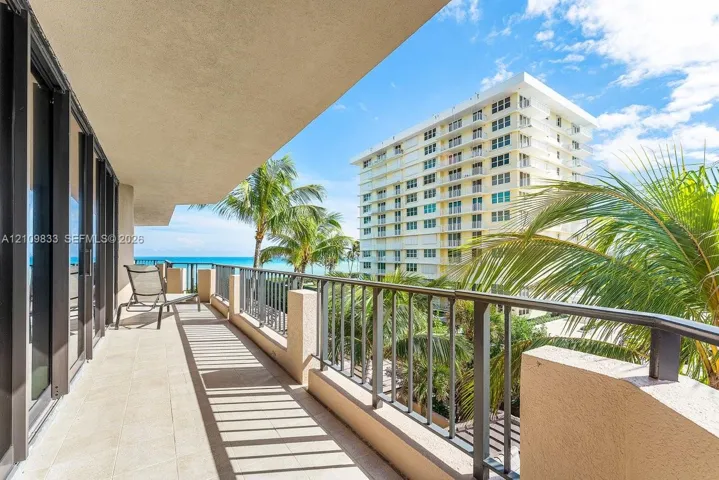 Covered balcony featuring tile flooring and metal railings, overlooking palm trees and the ocean