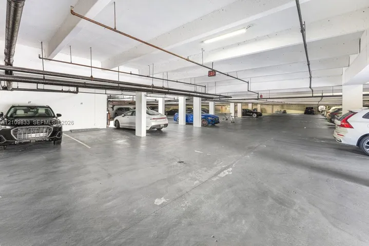 Covered parking garage featuring concrete flooring, structural support columns, and overhead linear lighting fixtures