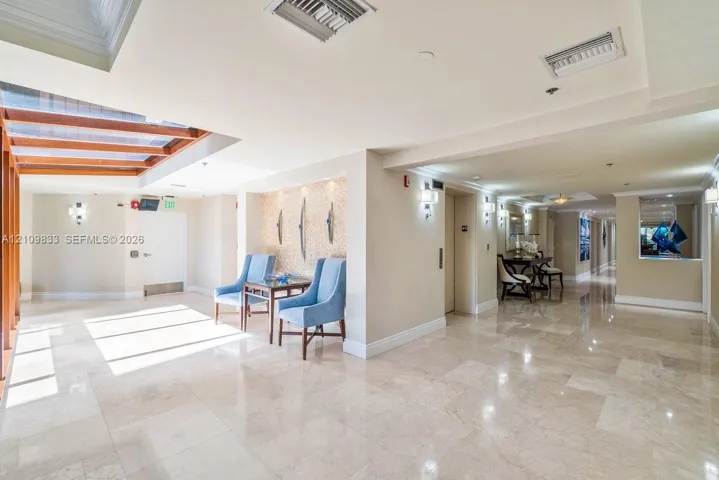 Polished stone flooring, recessed ceiling lighting, wall-mounted light fixtures, and a decorative recessed niche with textured detailing
