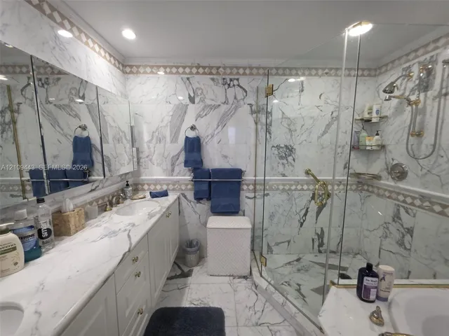 Bathroom featuring full-height stone wall tiling, a double vanity with stone countertop, recessed lighting, and a walk-in glass-enclosed shower with gold-tone hardware