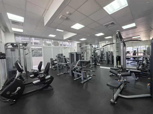 Fitness center featuring recessed square lighting, wall-to-wall mirrors, rubberized flooring, and expansive windows