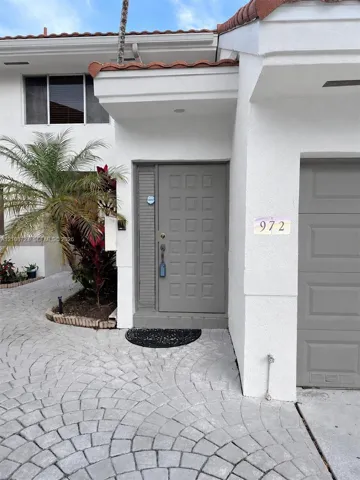 Stucco exterior featuring a tiled roof, gray paneled front door, and a patterned stone-paver driveway