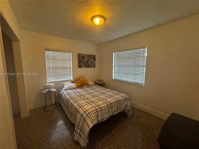 Room featuring neutral-toned walls, terrazzo flooring, two windows with horizontal blinds, and a dome-style flush-mount ceiling light