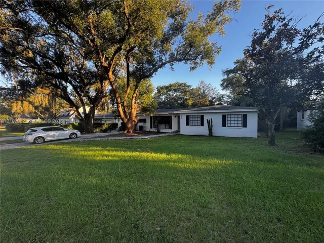 Single-story exterior featuring painted masonry siding, multi-pane window shutters, a gravel driveway, and mature landscaping