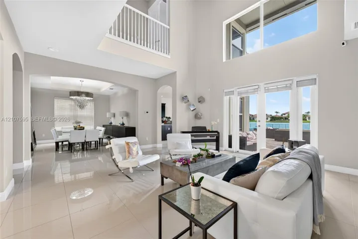 Double-height living area featuring large windows, polished tile flooring, arched doorways, and a mezzanine balcony with a white railing