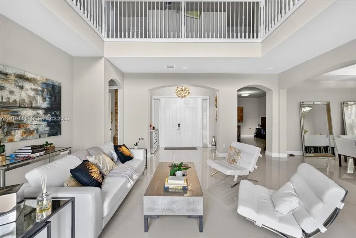 Double-height foyer featuring a mezzanine overlook, polished tile flooring, arched entryways, and double front doors