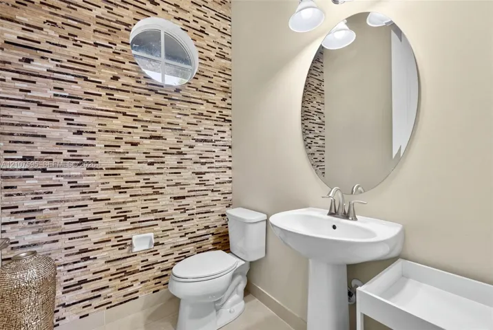 Stacked stone accent wall, oval wall-mounted mirror, white pedestal sink with polished nickel faucet, and circular window
